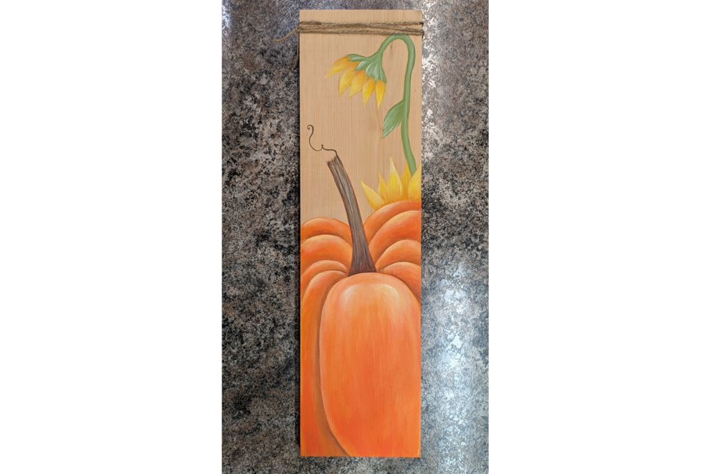 A photo of a fall pumpkin painting project that has a pumpkin and yellow flower painted on a board.
