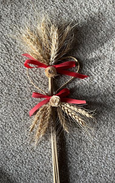 A photo of wheat weaved into an art piece with red ribbon.